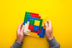 hand stacking up the colorful plastic block on yellow background photo