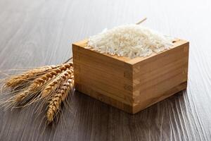 Uncooked dry Thai jasmine rice in box are overflow on wooden background photo