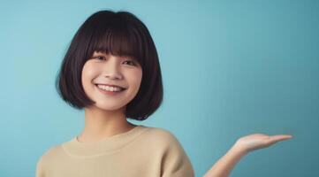Young woman with a friendly gesture. A cheerful young Asian woman with a bob haircut, presenting with her hand against a blue background. photo