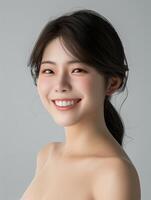 Radiant young woman with a joyful smile. Close-up portrait of a radiant young Asian woman with a joyful smile and dark hair, on a soft gray background. photo
