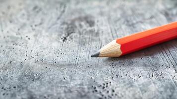 Pencil on textured surface. Close-up shot of an orange pencil laying on a rough, textured grey background. photo