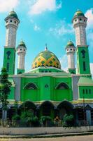 Green mosque with trees in the yard and bright blue sky photo