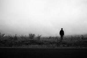 un hombre solo en el lado de el la carretera en brumoso clima, mirando triste y pequeño foto