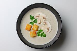 Mushroom cream soup with cream, croutons and herbs on a white wooden background. Delicious comfort food photo