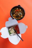 Noodles with pork and vegetables in take-out box on wooden table photo