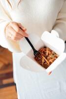 Fideos con carne de cerdo y verduras en caja para llevar sobre mesa de madera foto