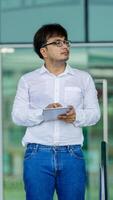 A man wearing a white shirt and glasses is holding a tablet in his hand photo