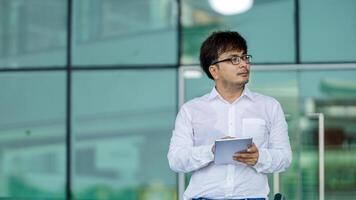 A man wearing a white shirt and glasses is holding a tablet in his hand photo