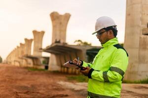 A man in a yellow jacket is writing on a clipboard while standing in front of a bridge. Concept of work and productivity photo