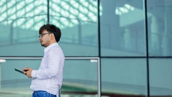 A man wearing a white shirt and glasses is holding a tablet in his hand photo