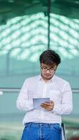 A man wearing a white shirt and glasses is holding a tablet in his hand photo