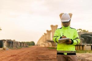 A man in a yellow jacket is writing on a clipboard while standing in front of a bridge. Concept of work and productivity photo