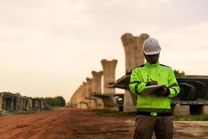 A man in a yellow jacket is writing on a clipboard while standing in front of a bridge. Concept of work and productivity photo