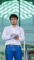 A man wearing a white shirt and glasses is holding a tablet in his hand photo