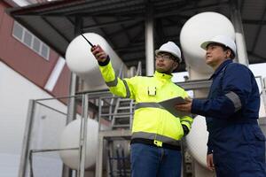 Two worker people wearing safety gear and holding a tablet to check product quality. One of them is smiling. Scene is positive and friendly in the manufactory. photo