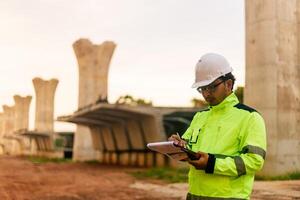 A man in a yellow jacket is writing on a clipboard while standing in front of a bridge. Concept of work and productivity photo