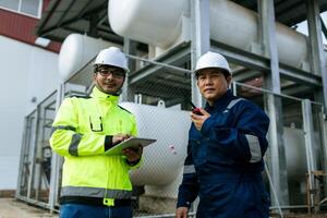 Portrait of two happy workers of metal stock in orange helmets and gray uniform standing together, posing and looking at camera. photo