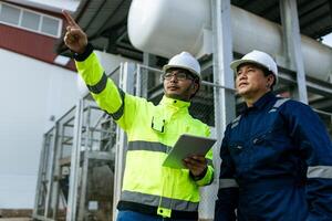 Two men are standing in front of a building, one of them pointing at a laptop. They are wearing safety gear and seem to be discussing something important photo