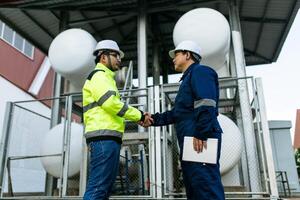 Two men in safety gear shake hands. One of them is holding a tablet. Scene is professional and friendly photo