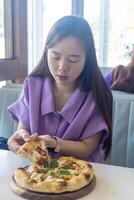 A woman is eating a pizza with her hands. The pizza is on a wooden plate. The woman is wearing a purple shirt photo