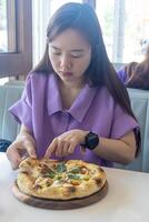 A woman is eating a pizza with her hands. The pizza is on a wooden plate. The woman is wearing a purple shirt photo