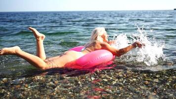 zee zomer vakantie gelukkig vrouw drijft Aan een opblaasbaar donut matras, roze zwemmen ring. zomer reizen vakantie vakantie Aan de zee. video