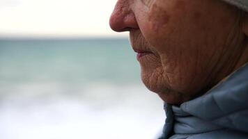 ein Frau ist Stehen auf ein Strand halten ein Becher. sie ist tragen ein Weiß Hut und ein Blau Jacke. das Szene ist Ruhe und friedlich, mit das Ozean im das Hintergrund. video