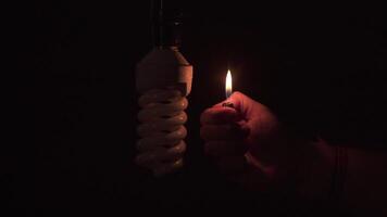 Man's hand holds a lit lighter, illuminating an unlit light bulb without electricity against black background video