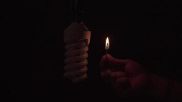 Man's hand holds a lit match, illuminating an unlit light bulb with no electricity against black background video