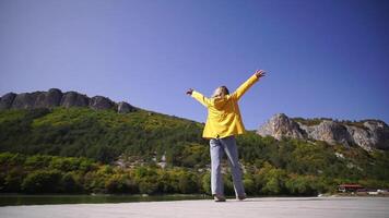 un' giovane donna nel un' giallo giacca è a piedi su un' sentiero vicino un' lago video