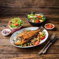 fried fish carp and fresh vegetable salad on wooden table photo