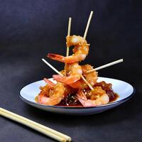 shrimp sauteed in garlic and soy caramel in stick served on a plate black background photo