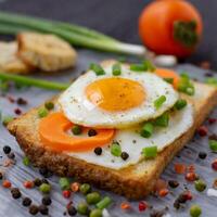 A fried egg laying on a toast topped with pepper seeds with carrots and spring onions photo