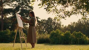 Creative woman artist paints a picture with a brush while standing near the easel in nature. Woman Artist, Art for Sales, Inspiration in Nature. video