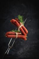 Dried pork sausages on a metal fork. Kabanos Close up on a black background. photo