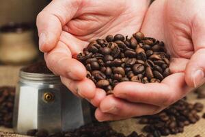 Hands holding roasted coffee beans on burlap and coffee background. Focus on beans. Close up. photo