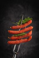 Dried pork sausages on a metal fork. Kabanos Close up on a black background. photo