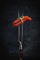 Dried pork sausages on a metal fork. Kabanos Close up on a black background. photo