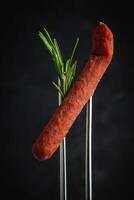 Dried pork sausages on a metal fork. Kabanos Close up on a black background. photo