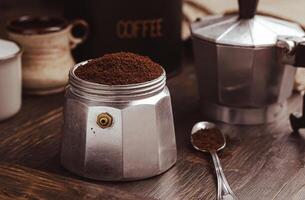 Moka coffee pot filled with brown ground coffee on dark wooden board, prepare to brewing Italian espresso. photo