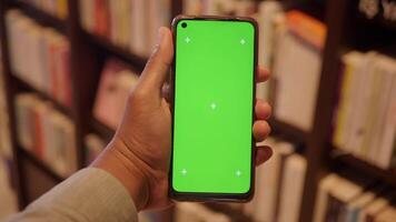 holding smart phone with green screen against library background video