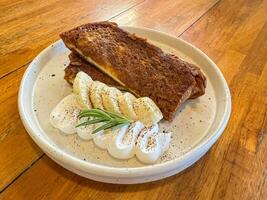 delicioso Tiramisu francés brindis con Fresco crema y arce jarabe. sabroso desayuno escena o postre con tostada, plátano y en polvo azúcar. foto