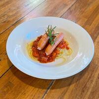 Hot dog or sausage stuffed with spaghetti in tomato pork sauce in white plate.Top view photo