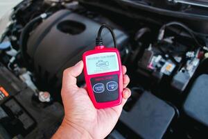 OBD2 or OBD scanner in a auto mechanic hand for engine system analysis with engine compartment blurred on background , Car maintenance service concept photo