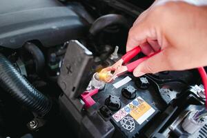 Car mechanic hand clamping red positive terminal cable clamp to car battery , Car maintenance concept photo