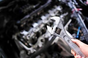 Adjustable wrench or adjustable spanner in a car mechanic hand with car engine blurred background , Car maintenance service concept photo