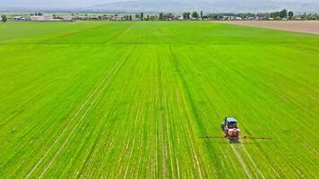 agricultural tractor spraying chemicals on green field with mountains on the horizon video