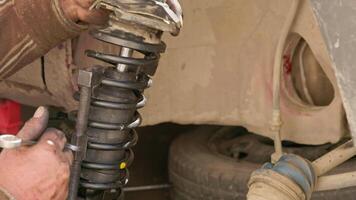 The calloused hands of a mechanic twist the coil spring ties with a wrench during DIY car repairs. video