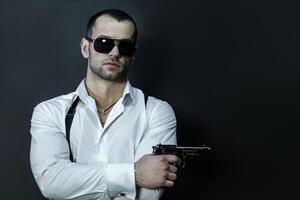 Young man in glasses wears holds a gun in his hand photo