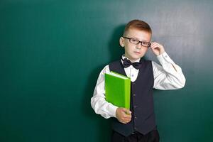 contento linda inteligente chico con un arco Corbata y en lentes con libro en su mano. primero hora a escuela. espalda a escuela. foto
